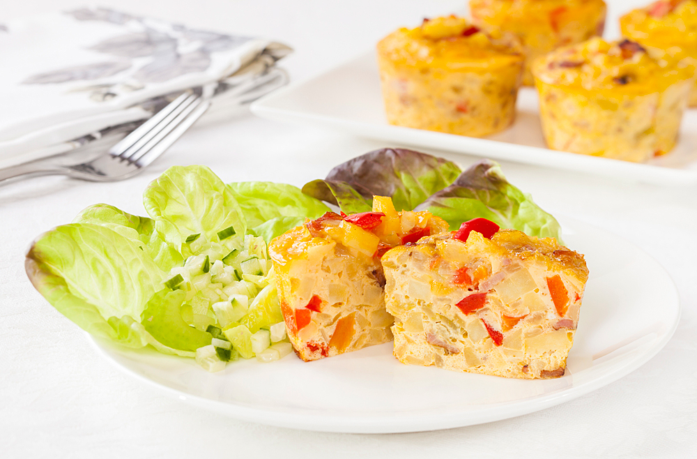 Close up of a small omelet made in a muffin tin. The omelet contains peppers and onions. 